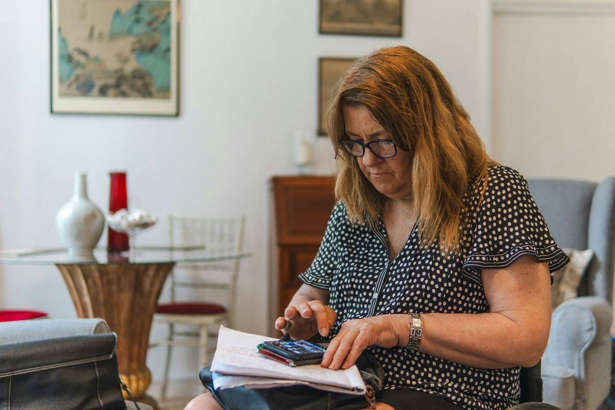 A woman works through a stack of papers with a calculator at her dining table