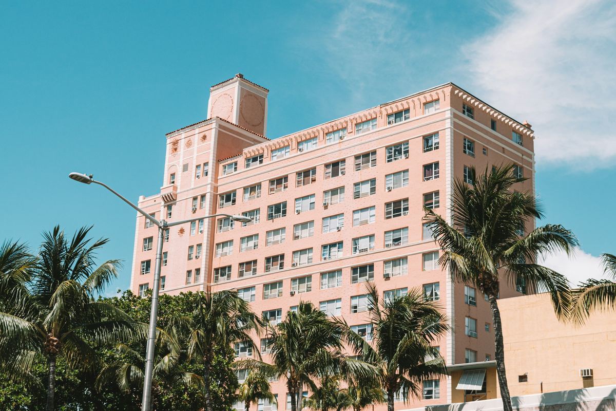 A pink apartment building framed by palm trees under a blue sky